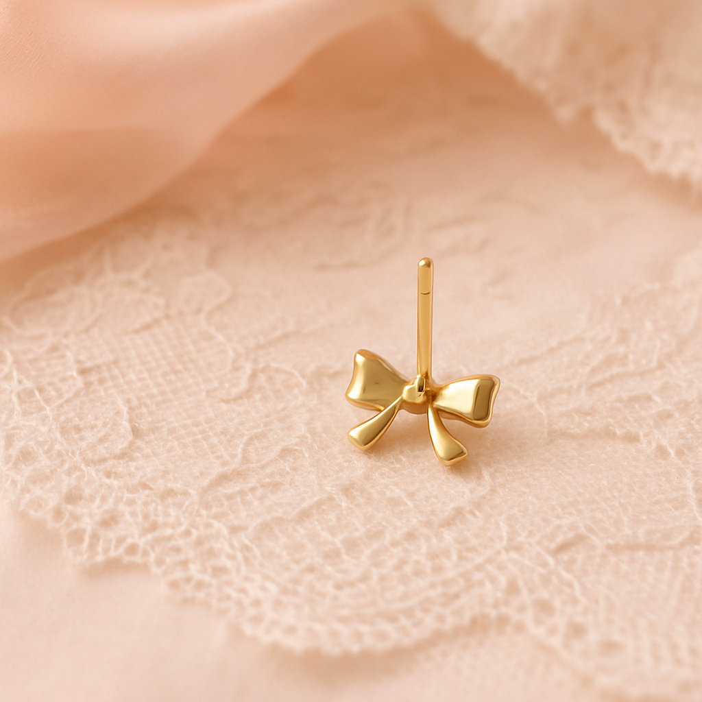 Gold bow-shaped earring on a soft pink fabric background backing