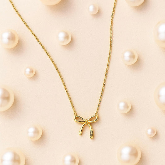 Gold bow necklace on a beige background with scattered pearls